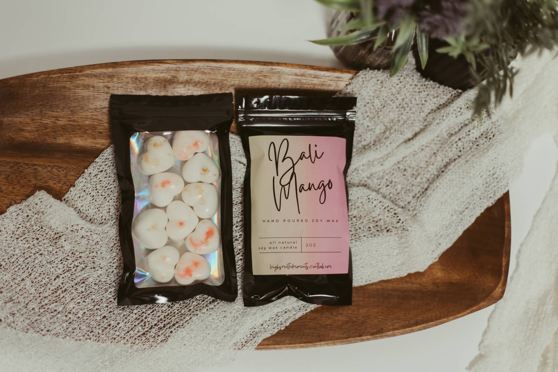 Bali Mango hand-poured soy wax melts in black resealable packaging on a wooden tray with a textured cloth.