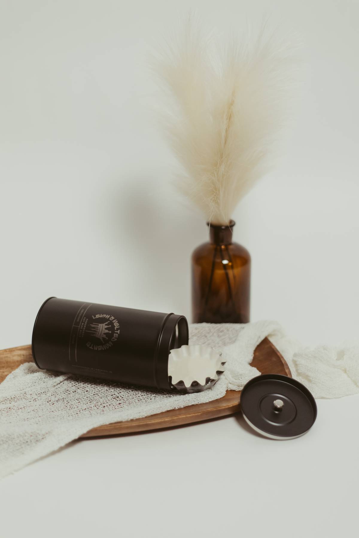 Black tin container with a removable lid and a reusable wax melt liner on a wooden tray with a neutral cloth.
