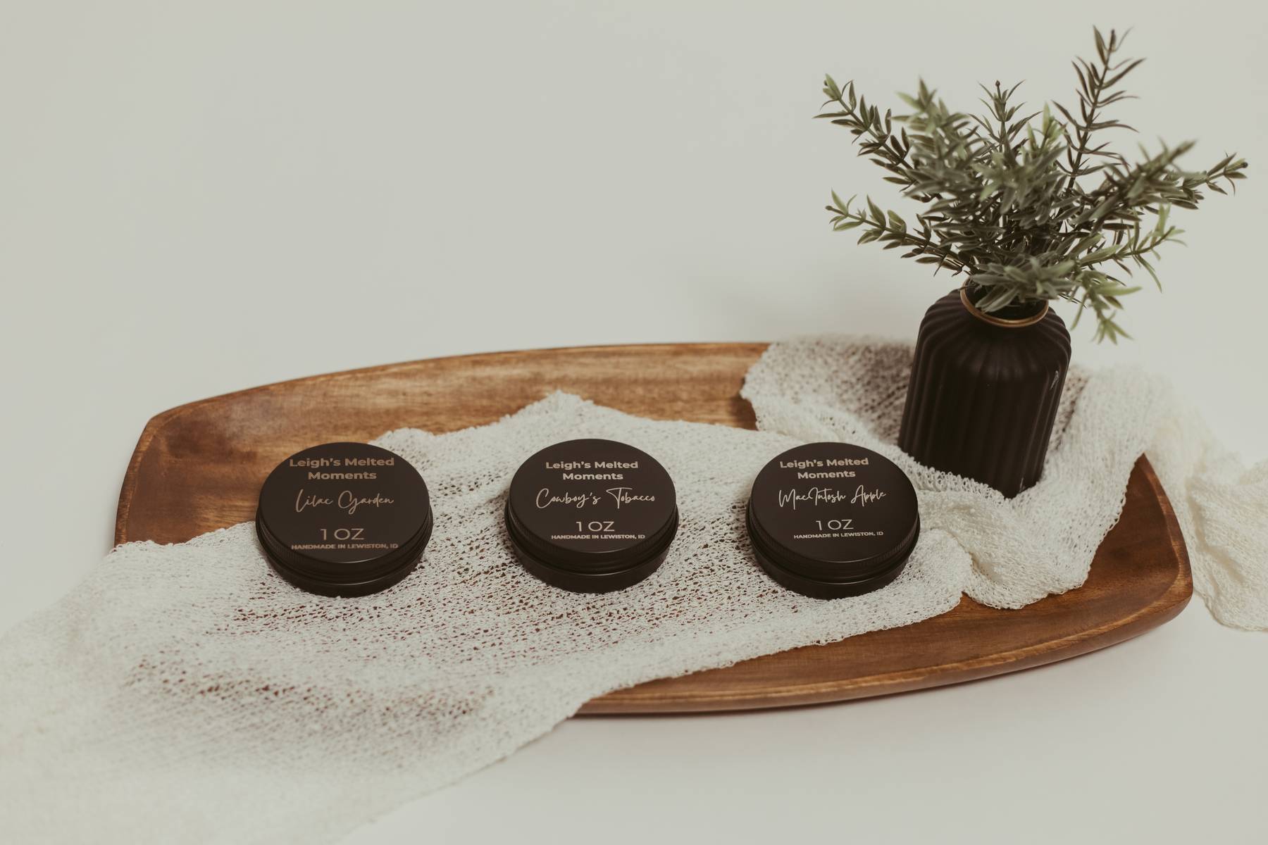 Three 1oz Leigh's Melted Moments wax melt containers on a wooden tray with a decorative plant.