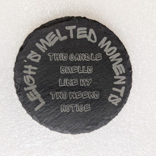 Round natural slate coaster with engraved text reading 'This candle smells like my two weeks' notice' and 'Leigh's Melted Moments' branding.