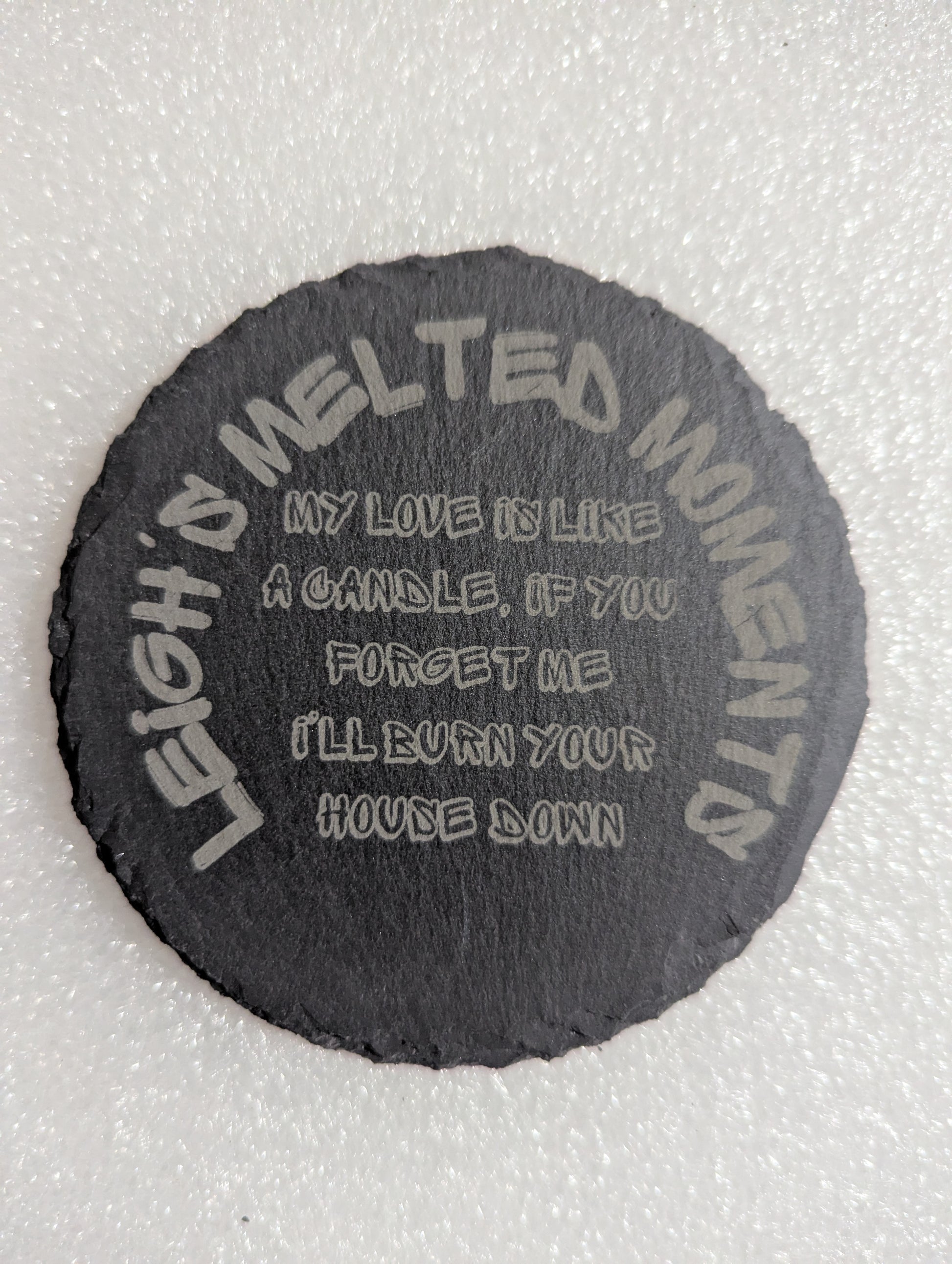 Engraved slate coaster with humorous text: 'My love is like a candle, if you forget me I'll burn your house down' and 'Leigh's Melted Moments' branding.